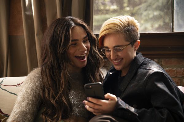 A transfeminine non binary person and transmasculine gender nonconforming person looking at a phone and laughing